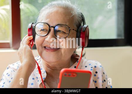 Alte asiatische Frau mit Brille lächelt fröhlich, während sie Musik mit Kopfhörern hört. Oldys Lifestyle-Konzept. Stockfoto