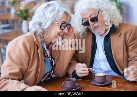 Lächelndes Seniorenpaar genießt gemeinsam Kaffee im Café im Freien in lässigen Outfits Stockfoto