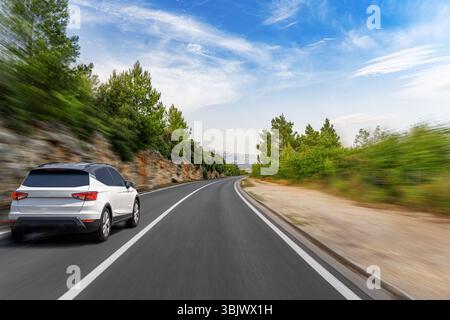 Ein dynamischer Low-Winkels erfasst einen modernen weißen SUV, der schnell auf einer kurvenreichen Küstenstraße fährt Stockfoto