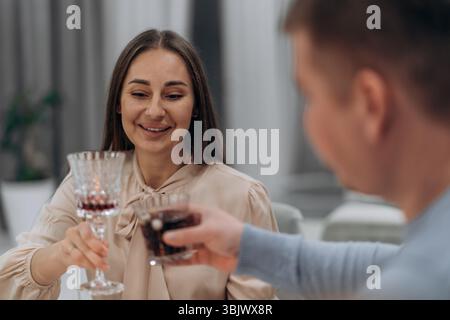 Lächelnde Frau und Mann heben die Gläser in sanftem Toast während des ruhigen Abends zu Hause und drücken Wärme Verbundenheit und Freude durch stille Feier aus Stockfoto