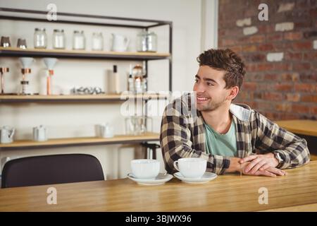 Weiße Keramikkkaffeetassen stehen auf einer Holztheke an der Kaffeebar mit Ziegelwand und Regalen Stockfoto