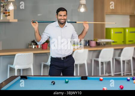 Asiatischer Mann, der Business Casual trägt, steht hinter blauem Billardtisch und hält Queuestift im Büro Stockfoto