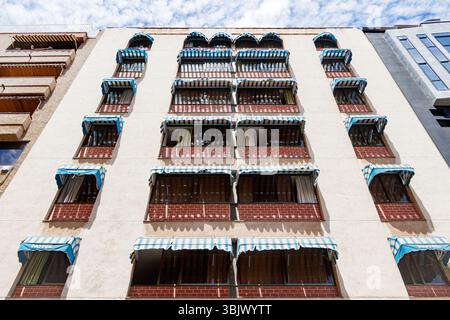 Blick auf die perspektivische Fassade eines städtischen Gebäudes mit Balkonen mit blau-weiß gestreiften Markisen vor klarem Himmel Stockfoto