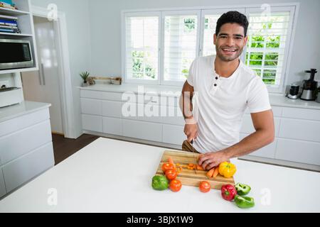 Hausmannskoch, der Karotten und Paprika auf dem Schneidebrett auf der Kücheninsel zerkleinert und den Mixer zeigt Stockfoto