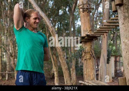 Mittelalter Mann, der Trizeps in grünem Hemd am Seilgarten zwischen Seilbrücken streckt, Kopierraum Stockfoto
