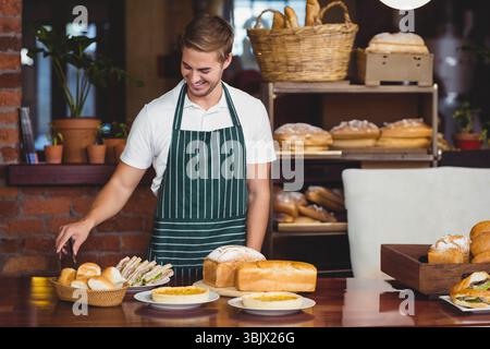 Brötchen liegen in Korb auf Holztheke mit Quiche-Törtchen und Sandwiches Stockfoto
