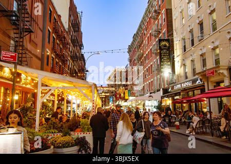 Überfüllte Maulbeerstraße, Little Italy in New York City mit beleuchteten Restaurants und Menschen, die das Abendambiente im Abendlicht genießen Stockfoto