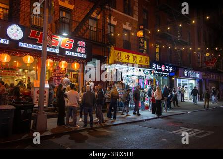 Nächtliche Szene in der mott Street, Chinatown New york City, mit Menschen, die in der Nähe von hellen Ladenfronten spazieren, die von bunten Schildern und Laternen beleuchtet werden Stockfoto