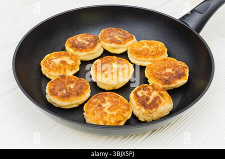 Eine Nahaufnahme köstlicher, goldbrauner Hüttenkäse-Pfannkuchen, bekannt als Syrniki, die in einer schwarzen Antihaftpfanne gekocht werden. Stockfoto