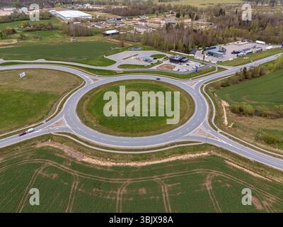 Tukums, Lettland - 26. April 2025: Luftperspektive eines Kreisverkehrs mit grünen Feldern und Gebäuden in einer ländlichen Landschaft Stockfoto