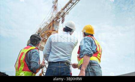 Eine Gruppe von Arbeitern auf der Baustelle diskutiert den Baufortschritt mit einem Turmkran im Hintergrund Stockfoto