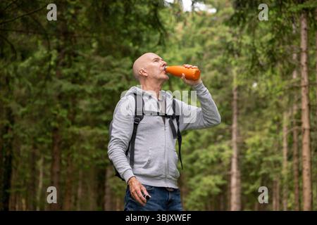 Ein Mann trinkt aus der wiederverwendbaren Flasche, während er in einem Wald wandert Stockfoto