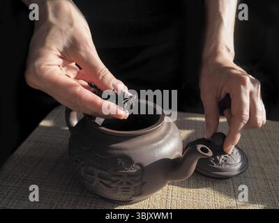 Lady schläft den Tee in einer Teekanne ein. Teekanne aus Ton. Teezeremonie. Tee in weiblichen Händen. Stockfoto