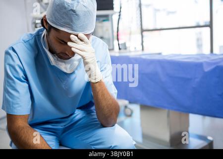 Asiatischer männlicher Chirurg, der auf dem Stuhl sitzt, mit Peelings, Maske, Handschuhen im OP, Kopierraum Stockfoto