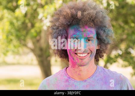 Lockiger erwachsener Mann grinst im Park mit puderbedecktem T-Shirt und Gesicht Stockfoto