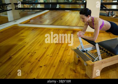 Die Pilates-Reformer-Maschine steht neben der Ballettbarre auf Holzboden und reflektiert im Studio-Spiegel Stockfoto