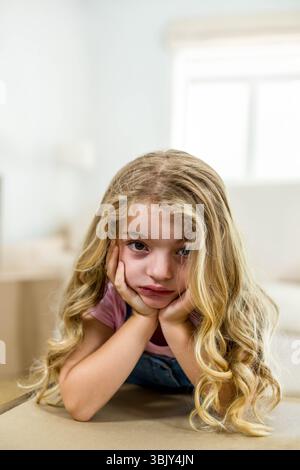 Das Kind lehnt sich auf den Tisch und blickt auf die Kamera neben der weißen Liege unter der Fensterbeleuchtung Stockfoto