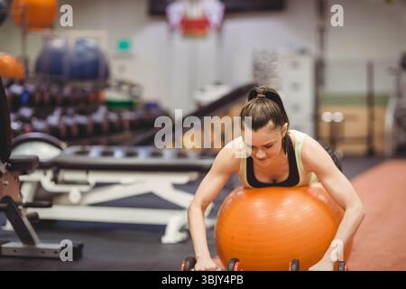 Weibliche Trainingsstabilitätsroutine im Fitnessstudio, gestützt auf orangen Balanceball und packende Kurzhanteln Stockfoto