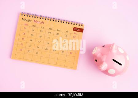 Brauner Schreibtischkalender für März 2026 und rosafarbene Schweinebank. Stockfoto