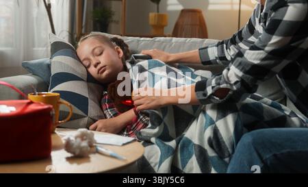 Kaukasische Familie zu Hause krank krank schlafendes Kind Mädchen Tochter Mutter Frau Mutter bedeckt Kind mit Decke berührend Stirn Temperatur überprüfen Fieber Stockfoto