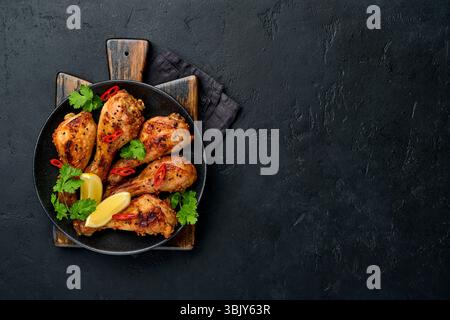Gegrillte Hähnchenschenkel oder gebratene grillgerichte mit Gewürzen und Tomatensalsa-Sauce auf einem schwarzen Teller. Draufsicht mit Kopierbereich. Stockfoto
