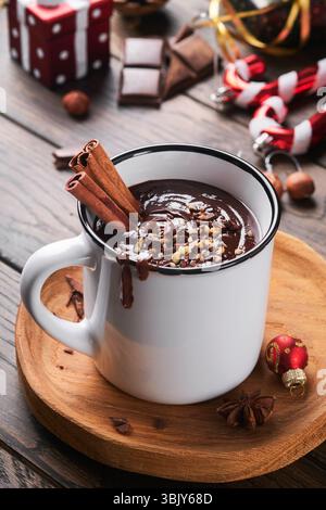 Heiße Schokolade. Hausgemachte scharfe heiße Schokolade mit Zimt, zerkleinerte Haselnuss in Emaille-Becher auf altem hölzernem Hintergrund. Gemütliche Saison Stockfoto