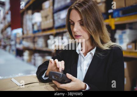 Mittelerwachsene Frau, die Geschäftskleidung trägt, Scannerkarton mit Handscanner im Lagerhaus Stockfoto