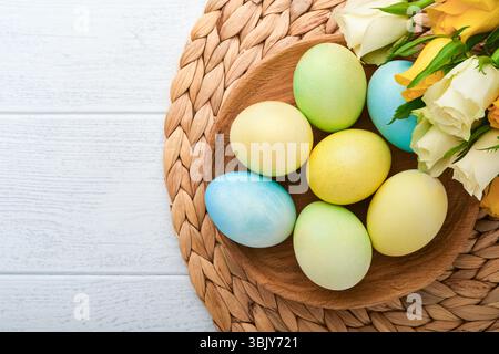 Frohe Ostern. Ostereier auf rustikalem Tisch mit weißen und gelben Rosen. Natürlich gefärbte bunte Eier in Holzteller und frühlingsflo Stockfoto
