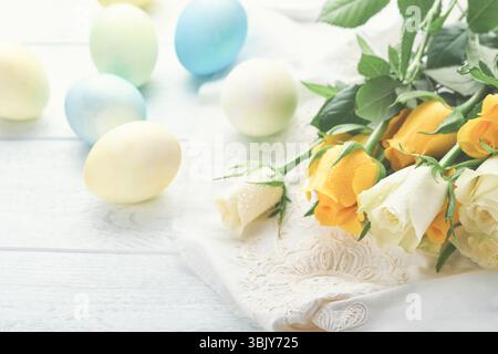 Frohe Ostern. Ostereier auf rustikalem Tisch mit weißen und gelben Rosen. Natürlich gefärbte bunte Eier in Holzteller und frühlingsflo Stockfoto