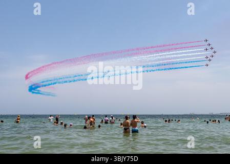 Rote Pfeile der Royal Air Force zeigen ein Team, das über den Mar Menor mit rot-weiß-blauem Rauchpfad fliegt. San Javier AIRE25 Airshow. Menschenmassen im Mittelmeer Stockfoto