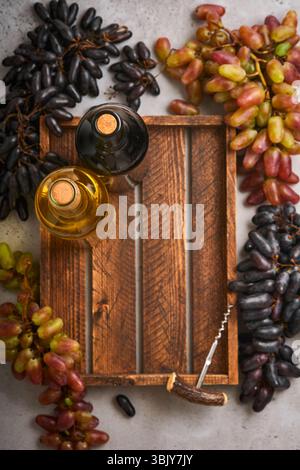 Zwei Weinflaschen mit Trauben und Weingläsern auf altem grauen Betontischhintergrund mit Kopierraum. Rotwein mit einem Rebzweig. Stockfoto
