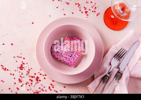 Valentinstag Tischeinstellung mit rosafarbenem Teller und Geschenkherz auf rosa hellem Hintergrund Stockfoto