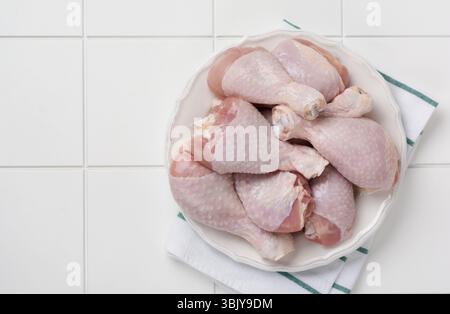 Rohe Hähnchenschenkel mit Tomatenkirsche, Kräutern, Basilikum und Gewürzen, auf weißem Marmorhintergrund, Kopierraum von oben. Gesund kochen Stockfoto