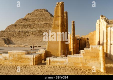 Zwei Touristen laufen vorbei an der Stufenpyramide von Djoser, dem ältesten kompletten Steinbaukomplex Ägyptens, der während der 3. Dynastie (ca. 2630–2611 v. Chr.) für Pharao Djoser erbaut wurde. Stockfoto