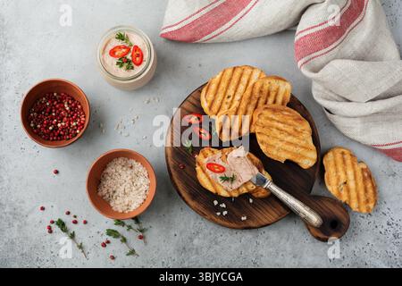 Hausgemachte Hühnerpastete aus Leber mit rotem Pfeffer, Thymianzweigen und gerösteten Brotscheiben auf altem Holzbrett auf grauem Beton oder s Stockfoto