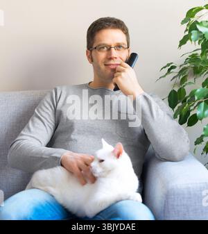 Menschen entspannen auf dem Sofa mit TV-Fernbedienung. Vor dem Fernseher mit seiner Katze. Stockfoto
