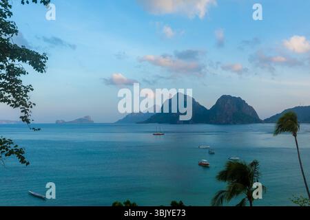 Ein malerischer Blick auf eine Bucht mit mehreren Booten, die auf dem Wasser segeln, umgeben von üppigen Bäumen und fernen Bergen, die die Ruhe und Schönheit eines tropischen Paradieses einfangen. Stockfoto