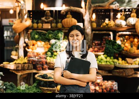 Lächelnder Unternehmer mit einem digitalen Tablet auf einem Markt im Freien. Asiatische Frau in einer Schürze, die in die Kamera schaut, während sie sich aufhält Stockfoto