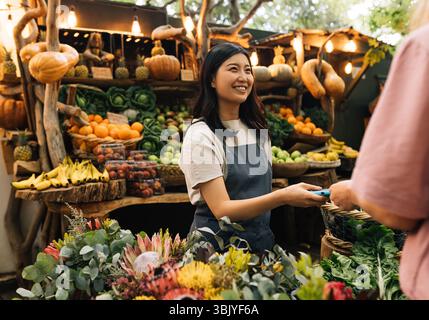 Anbieter, der Zahlungen auf dem Außenmarkt erhält. Eine Frau in einer Schürze, die auf einem Bauernmarkt arbeitet und Kunden ansieht. Stockfoto