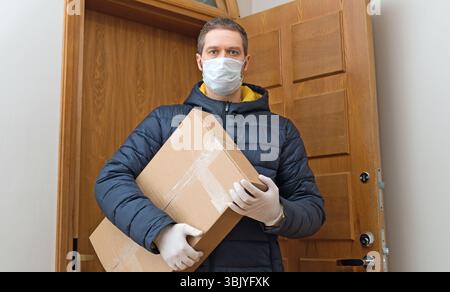 Männlicher Kurier in medizinischer Maske und Handschuhe mit Paket. Stockfoto