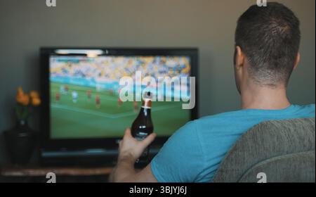Mann mit einer Flasche Bier, der im Fernsehen Fußball gucken konnte. Stockfoto