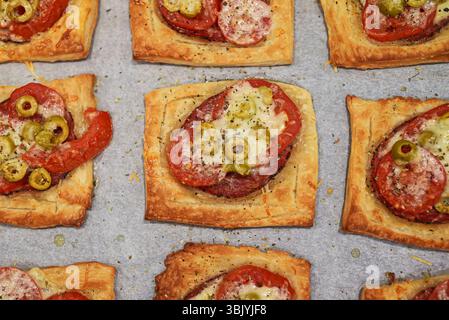 Gebackene quadratische Mini-Pizzas mit Salami, Käse, Oliven und Tomaten. Stockfoto
