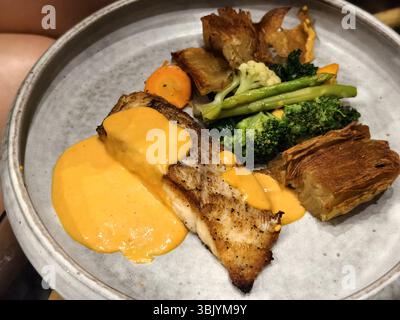 Gegrilltes Fischfilet mit samtiger Orangensauce, serviert mit knusprigen Kartoffeln, Brokkoli, Spargel, Karotten und Blumenkohl Stockfoto