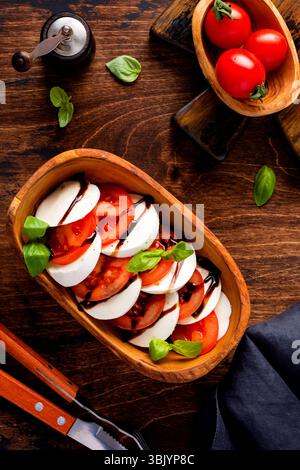 Caprese Salat italienische Küche mit Reifen Tomaten, frischem Gartenbasilikum und Mozzarella in Olivenholzschale auf altem rustikalem Backgürtel Stockfoto