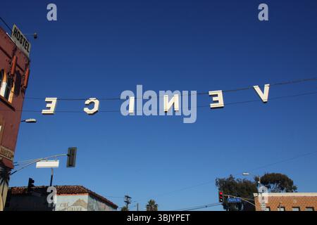 Das Schild „Venice“ hängt über der Pacific Avenue in Venice Beach, Kalifornien, und wird von hinten an einem sonnigen Tag mit tiefblauem Himmel und urbaner Umgebung betrachtet. Stockfoto