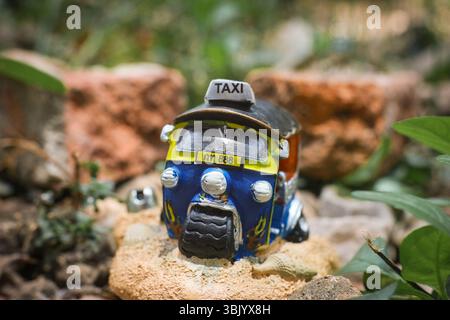 Nahaufnahme einer bunten Miniatur-Thai-Tuk-Tuk-Skulptur auf rustikalem braunem Stein mit weichem Hintergrund. Traditionelles ländliches thailändisches Transportkonzept. Stockfoto