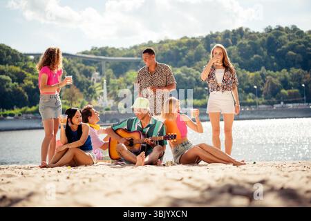 Eine Gruppe von Freunden, die einen Sommertag im Freien am sonnigen Ufer mit Musik und Lachen genießen Stockfoto
