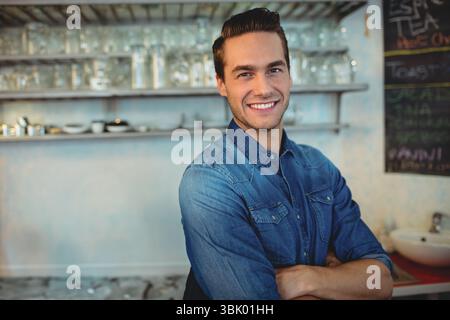 Metallregale, in denen saubere Glaswaren und Tassen an der Betonwand hinter der Theke aufbewahrt werden Stockfoto