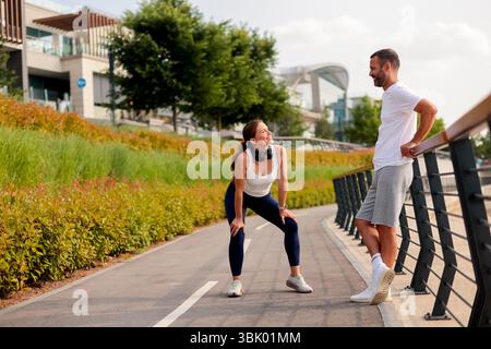 Zwei Freunde teilen sich während ihres Workouts einen lebendigen Moment und genießen Lachen und Gespräche in einem üppigen Stadtpark unter klarem blauen Himmel. Stockfoto