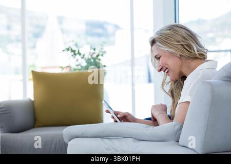 Frau lächelt beim Scrollen des Smartphones auf grauem Sessel im Wohnzimmer, Kopierraum Stockfoto